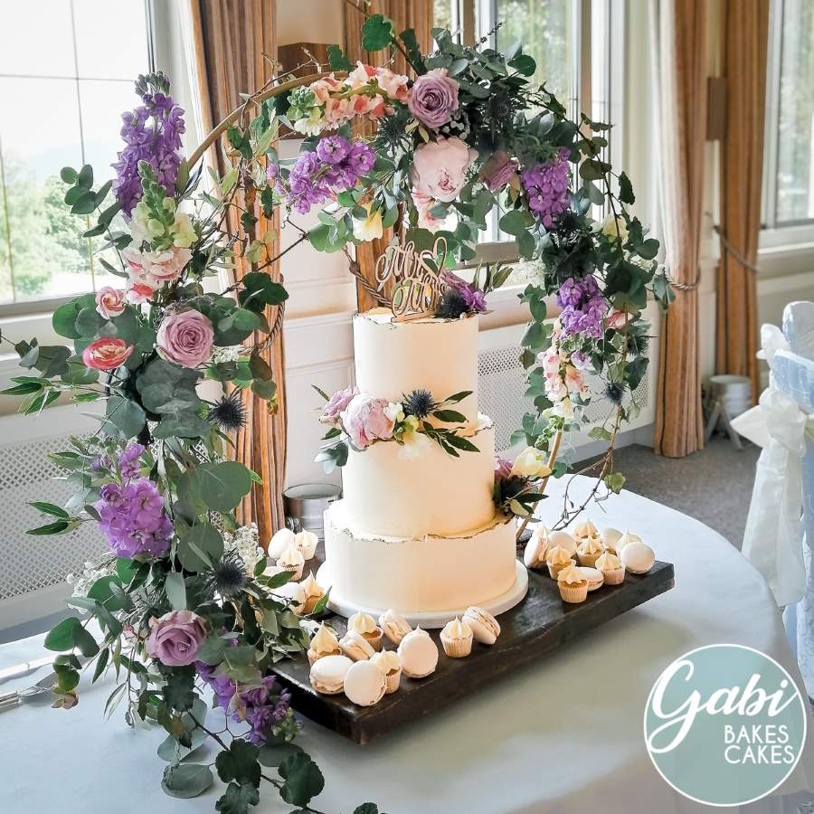 Three tier wedding cake within a hoop of fresh flowers.