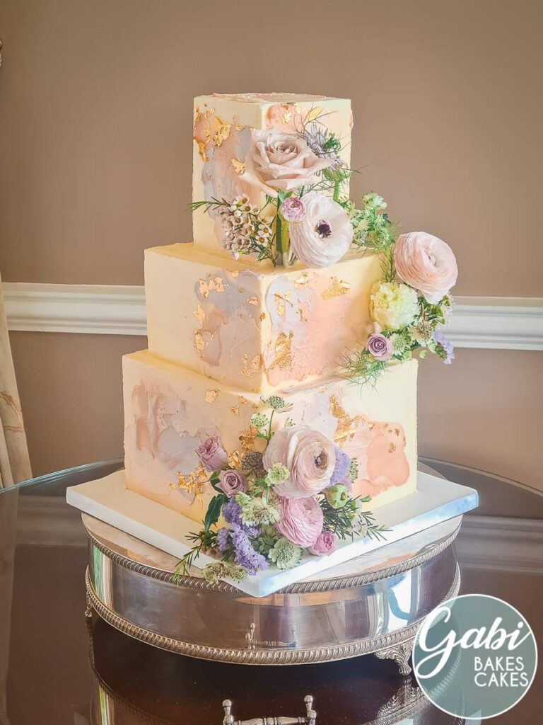 Square three tier wedding cake with gold leaf and pastel strokes.